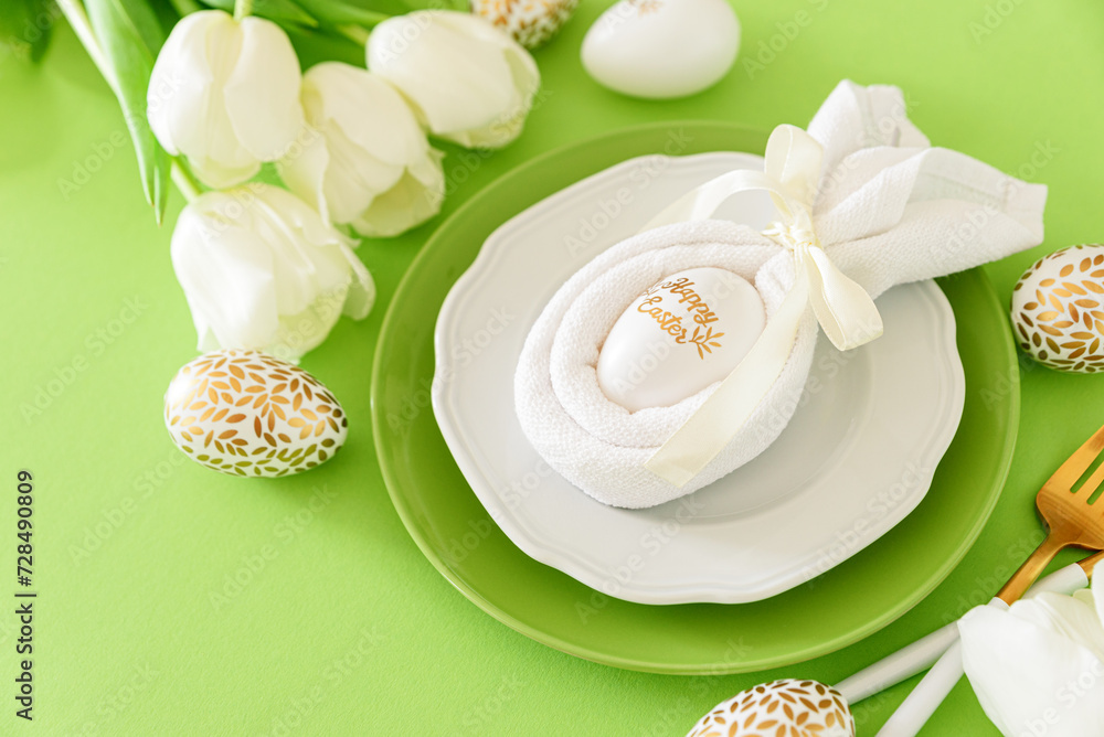 Plate decorated bunny ear napkin, white tulips and Easter eggs on green background. Easter celebration concept. Flat lay. Top view Plate decorated bunny ear napkin, white tulips and Easter eggs on green background. Easter celebration concept. Flat lay. Top view