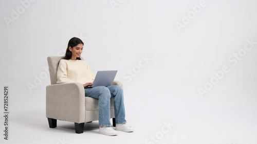 Positive Caucasian woman browsing on a laptop while sitting in a armchair on a white background. Online connection, internet communication, modern technology, freelance work concept. photo