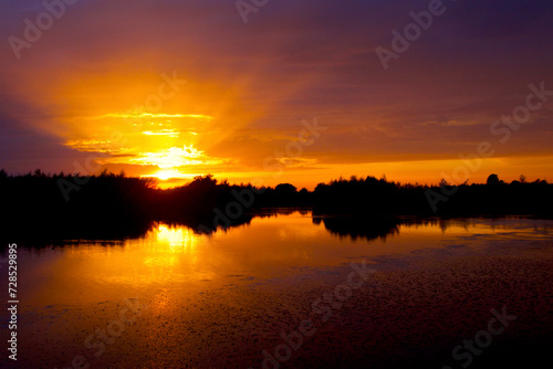 Sun rays shine through the clouds just before dusk at the lake © tiger2506