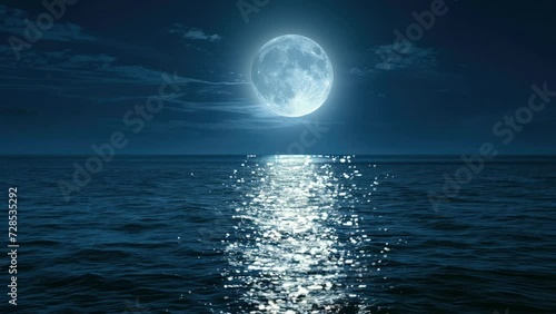 this large full blue moon rises brightly over the cloud bank in this calm ocean.