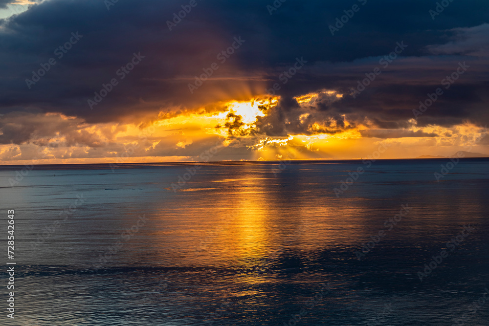 Sublime sunset piercing the clouds above the sea in Okinawa beach, Japan. Calm sea reflections, beautiful twilight and dramatic sky in horizontal image