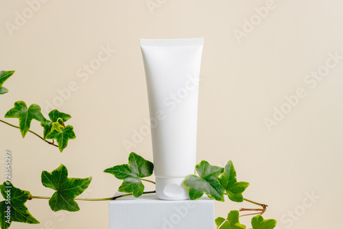Facial care cream with green plant leaves on podium at beige background. Natural organic skincare, body lotion, face cream. Mockup cream bottle for beauty products, aesthetic minimal style