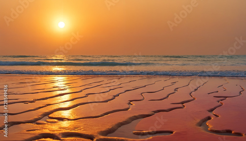 Serene sunset beach landscape with the sun going down over the water, waves, sand and an orange sky