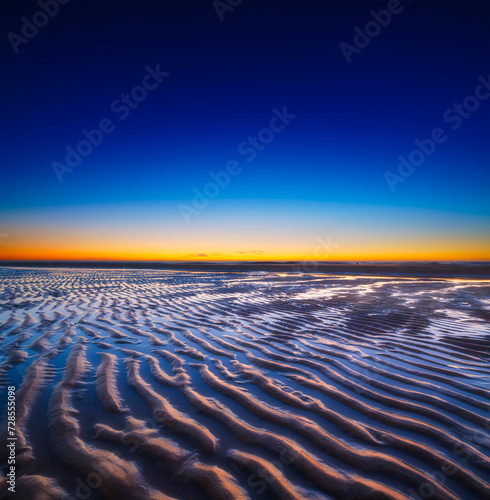 A seascape during sunset. Lines of sand on the seashore. Bright sky during sunset. A sandy beach at low tide. Wallpaper and background.