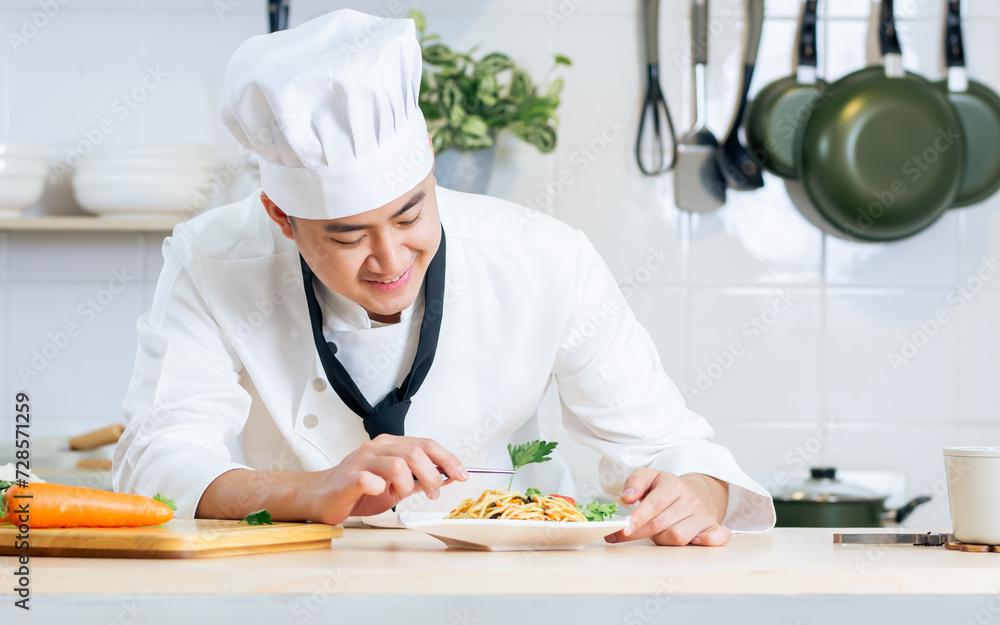 Portrait beautiful Asian professional male chef wearing white uniform, hat, holding, showing plate of spaghetti, cooking in kitchen, making surprising face with happiness. Restaurant, Food Concept.