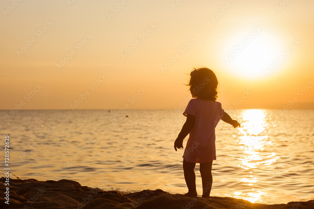 Little child on sand beach at sunset.