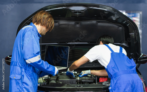 Two handsome male mechanics wearing uniform, using laptop, checking or inspecting for fix, repair car or automobile components, working in car maintenance service center or shop. Industry Concept.