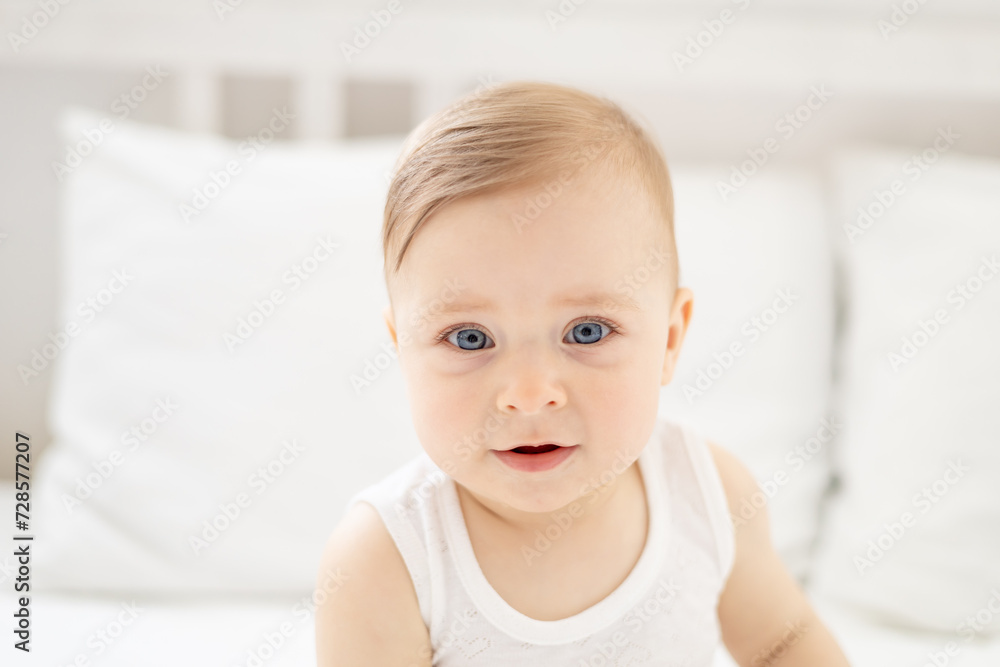 close-up portrait of a happy little baby girl or boy in a white bodice on the bed in the bedroom, a baby with blue eyes close-up portrait of a happy little baby girl or boy in a white bodice on the bed in the bedroom, a baby with blue eyes
