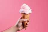 Hand holding ice cream cone over pink background