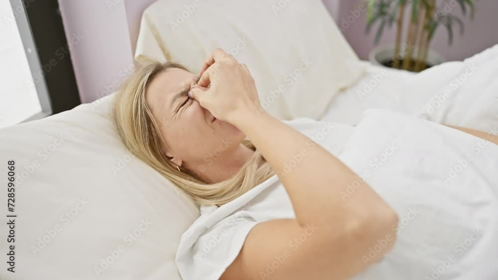 A tired blonde woman rubs her eyes as she wakes up in a cozy, bright bedroom A tired blonde woman rubs her eyes as she wakes up in a cozy, bright bedroom