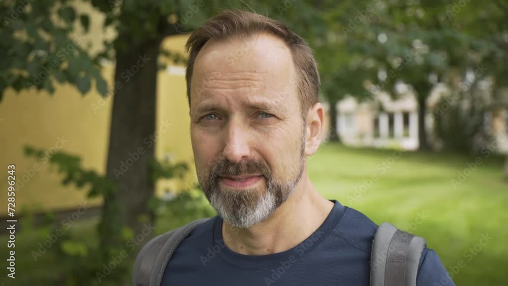 A handsome middle-aged Caucasian man with a backpack smiles at the camera - ends in closeup A handsome middle-aged Caucasian man with a backpack smiles at the camera - ends in closeup