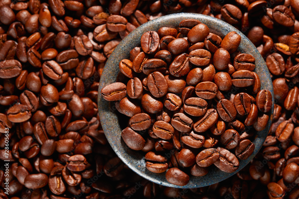 Fototapeta premium A bowl of roasted coffee beans in a pile of coffee beans. Top view. Studio shot.