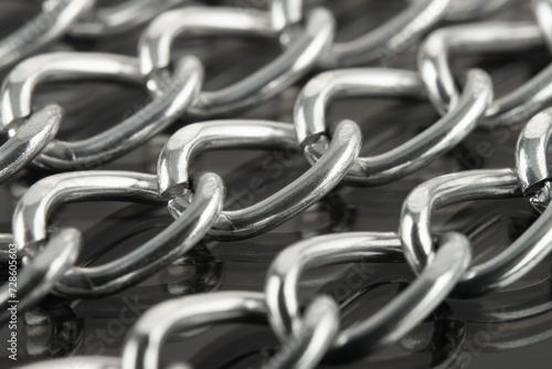 Close-up of metal chains stacked in a row on a reflective surface.
