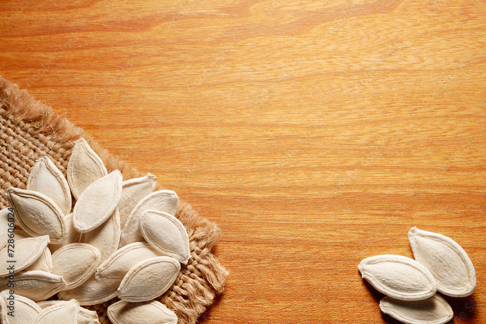 A small group of unshelled dried pumpkin seeds on a burlap cloth on a wooden background with copy space. Top view. A small group of unshelled dried pumpkin seeds on a burlap cloth on a wooden background with copy space. Top view.