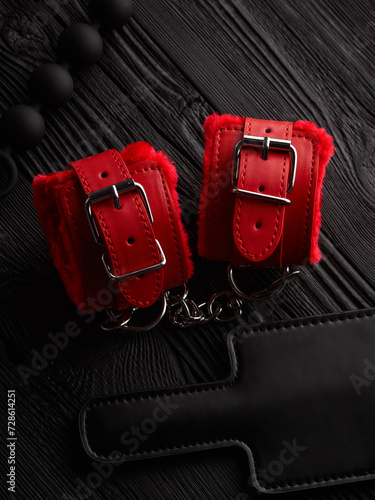 Red handcuffs and accessories for BDSM role play game over black wooden background