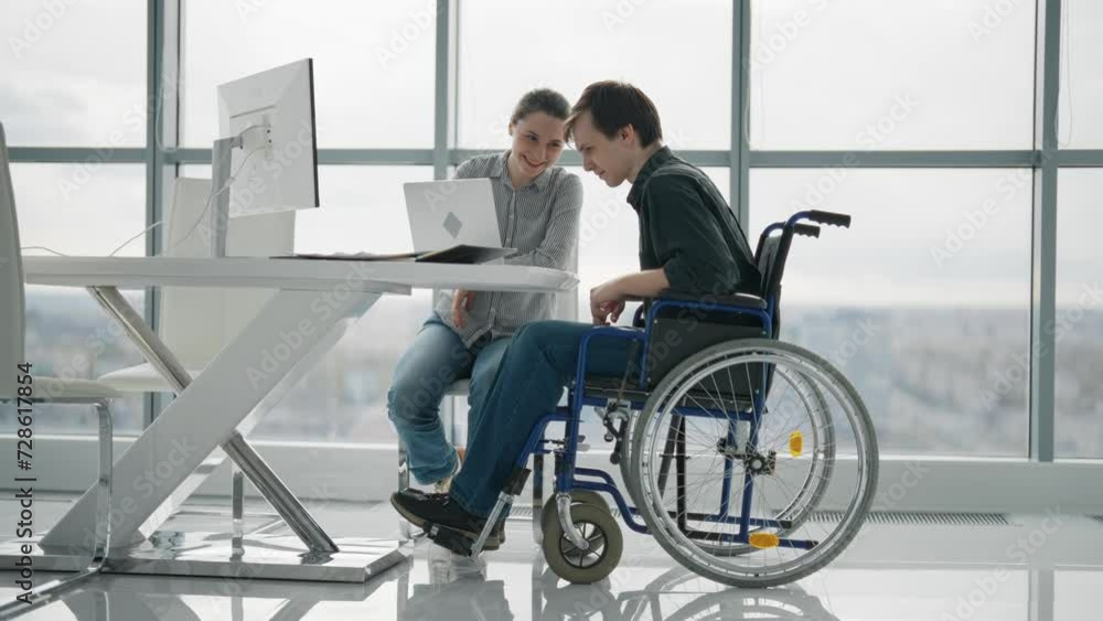 Colleagues, woman shows to man in wheelchair finance diagram document work together in office. Workers discuss analytics pie chart sit at desk. Usual life of people with physical disability concept. Colleagues, woman shows to man in wheelchair finance diagram document work together in office. Workers discuss analytics pie chart sit at desk. Usual life of people with physical disability concept.