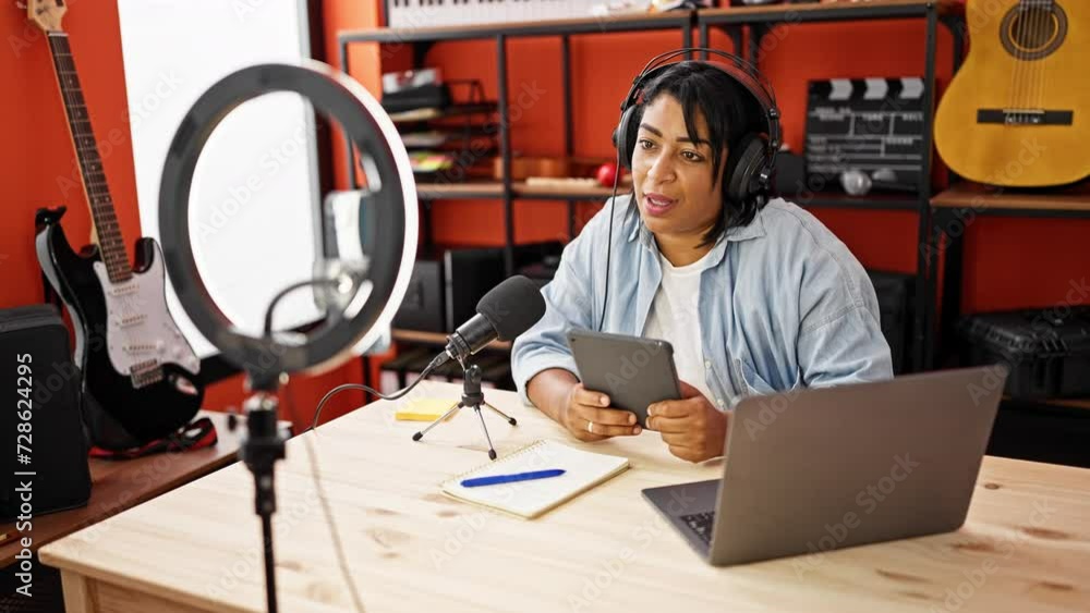 Smiling woman podcasting with microphone, tablet, and laptop in a music studio setup. Smiling woman podcasting with microphone, tablet, and laptop in a music studio setup.