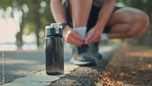 Closeup on black bottle of water, Blurred man tie their shoes before run or jogging on track race in the public park, Healthy photo