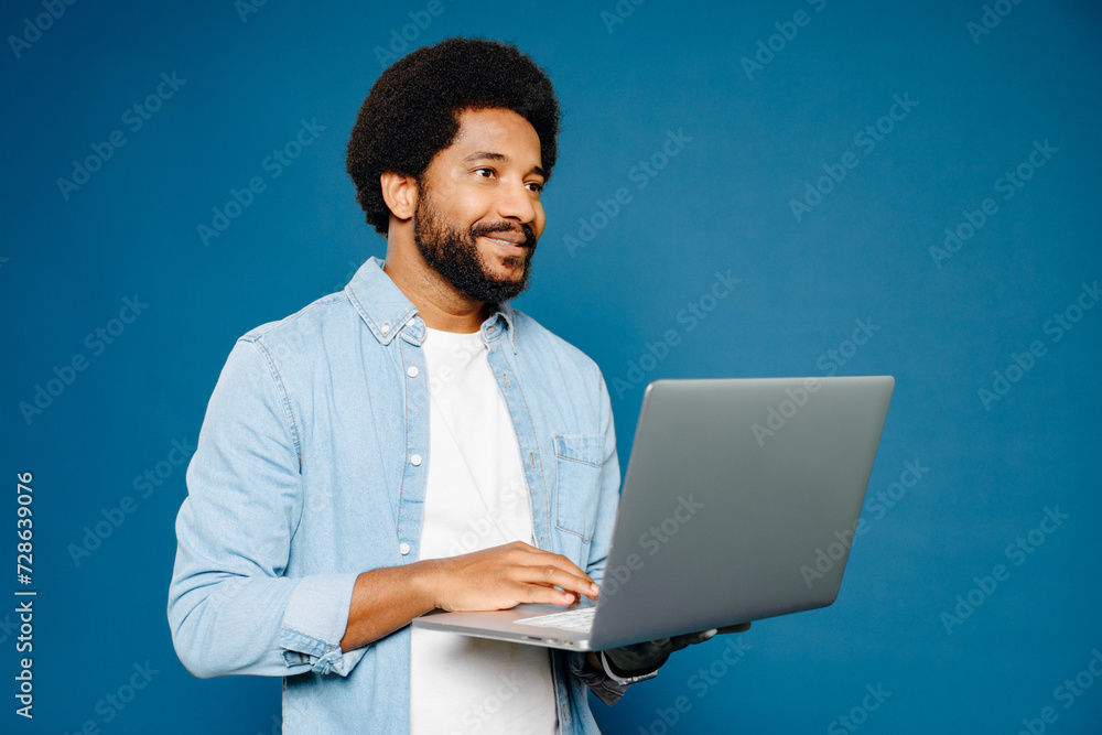 Smart and intelligent Brazilian man, freelancer or student, using laptop against the blue background conveys focus and digital engagement, concept of online learning or the startup mindset Smart and intelligent Brazilian man, freelancer or student, using laptop against the blue background conveys focus and digital engagement, concept of online learning or the startup mindset