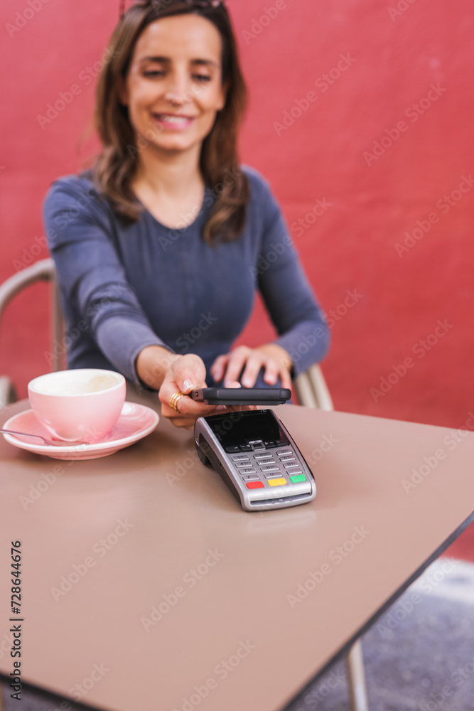 Happy woman paying with NFC technology as her mobile phone at payment terminal Happy woman paying with NFC technology as her mobile phone at payment terminal