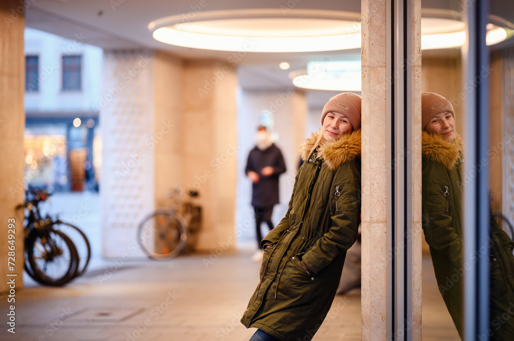 Fototapeta premium A young woman pauses for reflection in an urban passageway, her image mirrored in the glass