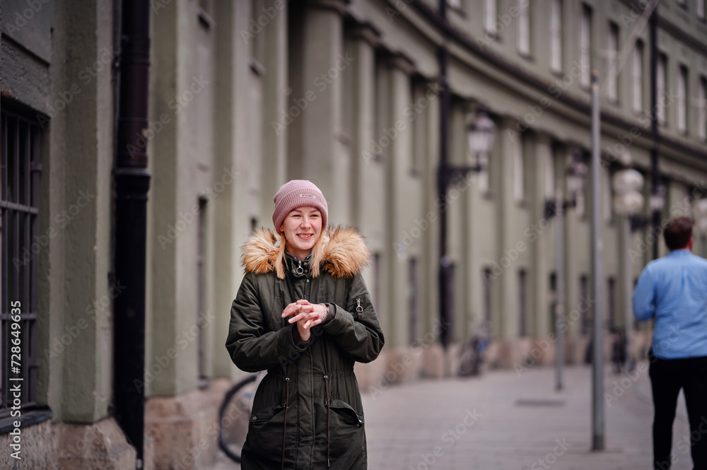 A woman stands crossed-armed and reflective on a cobblestone street, with city life softly blurred behind A woman stands crossed-armed and reflective on a cobblestone street, with city life softly blurred behind