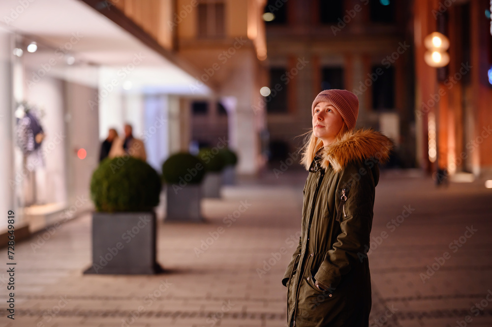 Obraz premium Young woman enjoys a serene walk past boutique windows on a beautifully lit city street at night