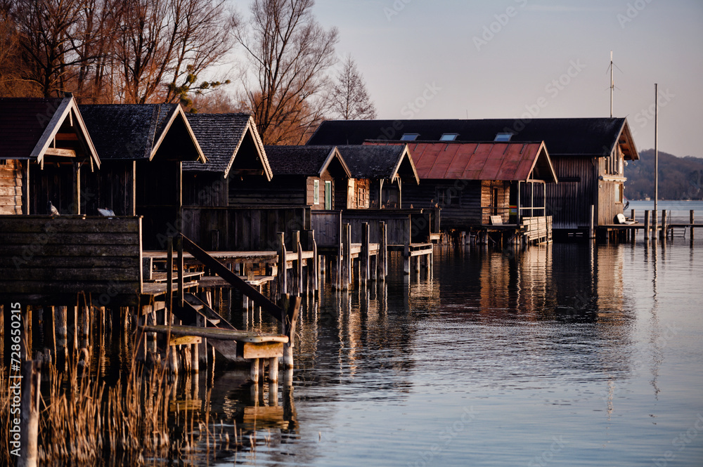 Obraz premium Evening light casts a glow on rustic boathouses lined along a tranquil lake