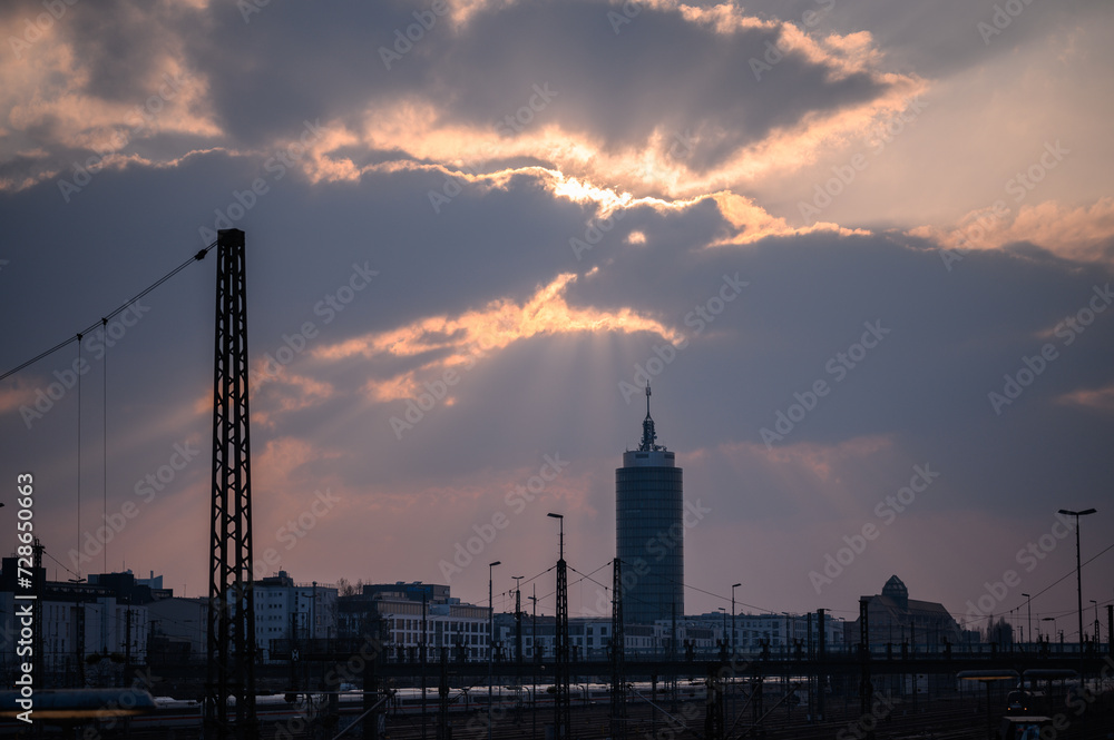 Sunbeams pierce through clouds above a silhouette of skyscrapers in an urban sunset