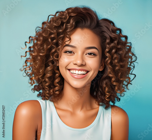 Portrait of a smiling happy beautiful young black african-american young woman with big curly hair wearing t-shirt on a light blue background.