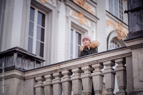 A pensive woman leans on a classic stone balcony, gazing out over the historic cityscape