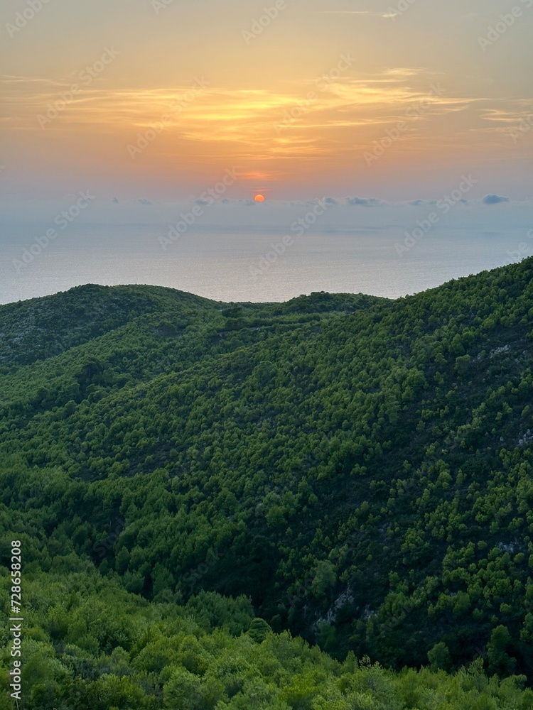 Mediterranean sunset from the Agalas viewpoint. Sitting and watching sunset in Zakynthos, Greece. Sunset pine trees, olive groves and sea view on a greek island.