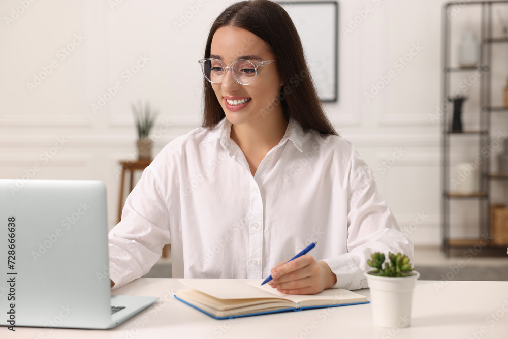 Young woman writing in notebook at white table indoors Young woman writing in notebook at white table indoors