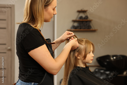 Professional hairdresser braiding girl's hair in beauty salon