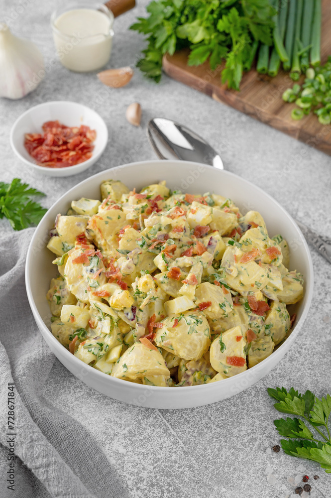 Salad of potatoes, eggs, bacon and fresh herbs with mayonnaise and yogurt dressing in a bowl on a gray concrete background. Salad of potatoes, eggs, bacon and fresh herbs with mayonnaise and yogurt dressing in a bowl on a gray concrete background.