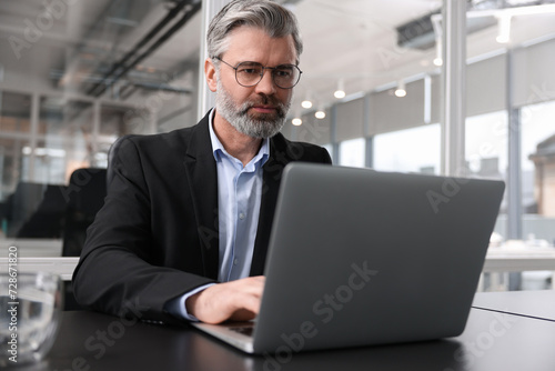 Handsome man working with laptop at table in office. Lawyer, businessman, accountant or manager