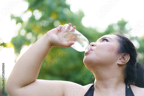 Happy Asian oversize fat woman drinking a water from bottle during taking a break after have a run.