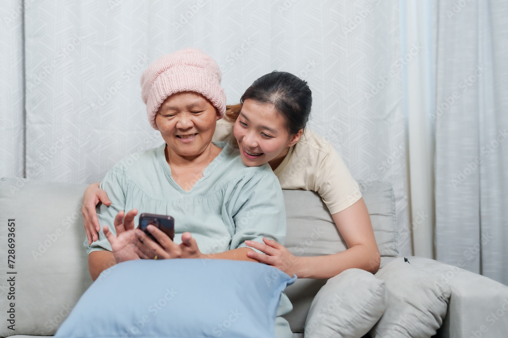 Sharing a digital moment, a daughter shows her mother something amusing on the phone, sparking laughter. woman in a knit cap laughs with her daughter at a phone screen, a light-hearted moment at home Sharing a digital moment, a daughter shows her mother something amusing on the phone, sparking laughter. woman in a knit cap laughs with her daughter at a phone screen, a light-hearted moment at home