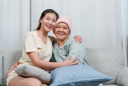 beaming daughter sits with her ailing mother, sharing a joyful moment, faces touched by smiles. Joy and resilience shine as a young woman and her mother with cancer share a close, happy connection © Ekkasit A Siam