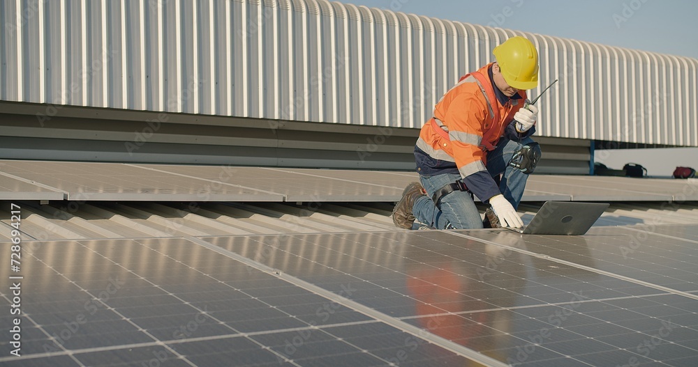 Technician engineer worker in high visibility vest and safety helmet inspecting solar panels with laptop on a roof Technician engineer worker in high visibility vest and safety helmet inspecting solar panels with laptop on a roof