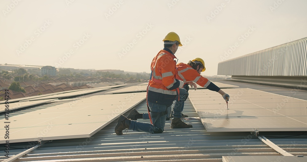 Two engineer workers in safety gear install solar panels on a rooftop, with a suburban landscape stretching out in the distance Two engineer workers in safety gear install solar panels on a rooftop, with a suburban landscape stretching out in the distance
