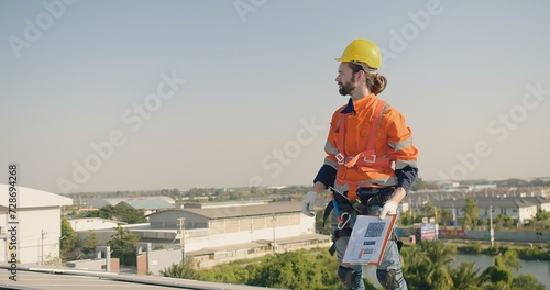 A solar technician with a clipboard inspects solar panels on a rooftop