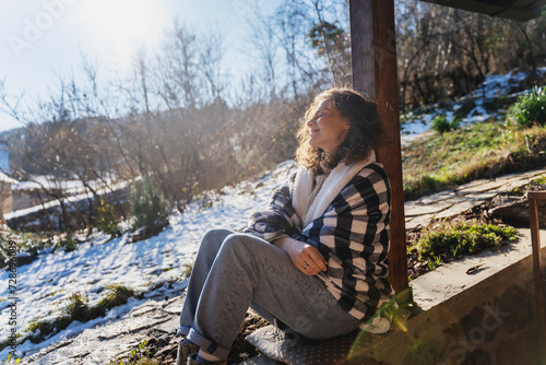Bilde på lerret Young smiling woman in a warm blanket on the terrace of a country house enjoying