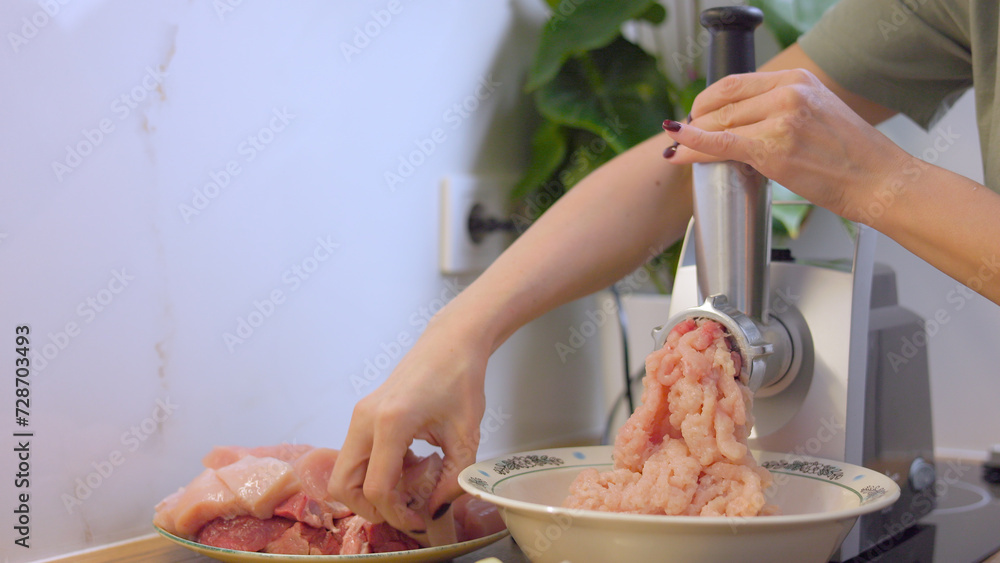 A young woman makes minced meat in a meat grinder