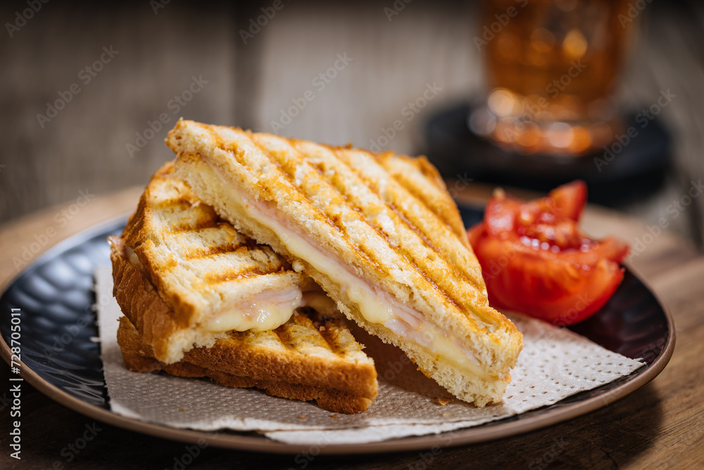 Toast sandwich with gouda cheese and turkey ham on a wooden background with ingredients in blurry background. Served with ice tea.