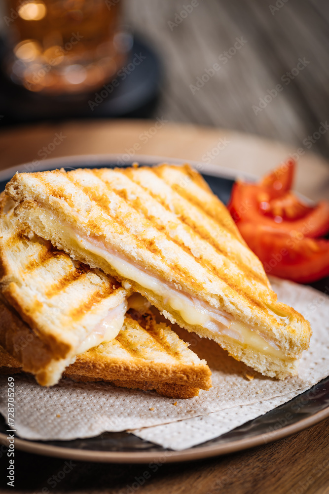 Toast sandwich with gouda cheese and turkey ham on a wooden background with ingredients in blurry background. Served with ice tea. Toast sandwich with gouda cheese and turkey ham on a wooden background with ingredients in blurry background. Served with ice tea.
