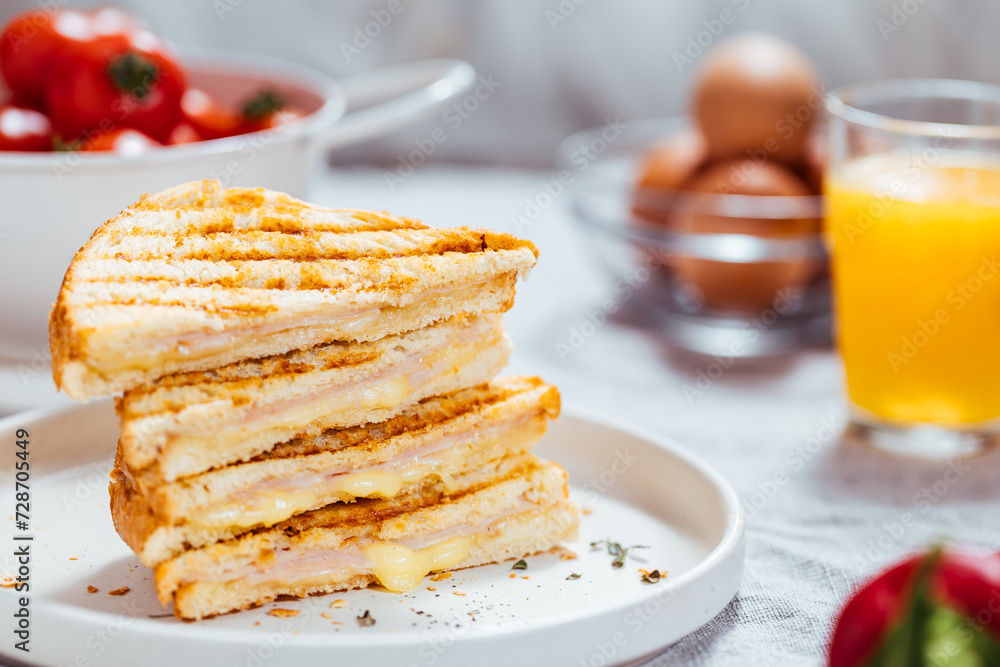 Toast sandwich with gouda cheese and turkey ham  on a bright background with ingredients in blurry background. Served with orange juice  and eggs