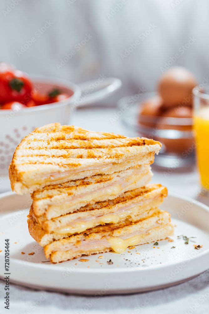 Toast sandwich with gouda cheese and turkey ham on a bright background with ingredients in blurry background. Served with orange juice and eggs Toast sandwich with gouda cheese and turkey ham on a bright background with ingredients in blurry background. Served with orange juice and eggs