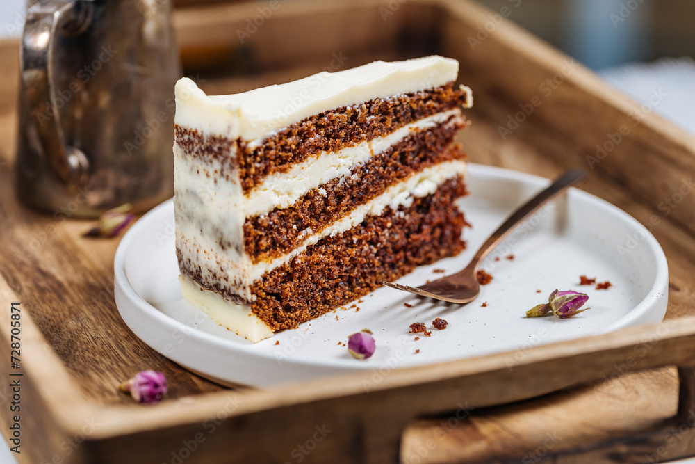 A piece of carrot cake served on rustic plate placed on bright sunny scene. Layered cake with cream cheese frosting and fluffy biscuit. Served with tea. A piece of carrot cake served on rustic plate placed on bright sunny scene. Layered cake with cream cheese frosting and fluffy biscuit. Served with tea.