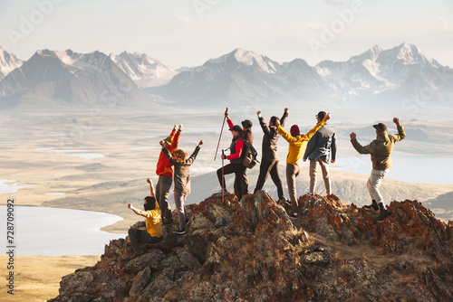 A large group of diverse tourists celebrates the completion of their climb to the top of the mountain with great view at sunset. Mixed ages and skills